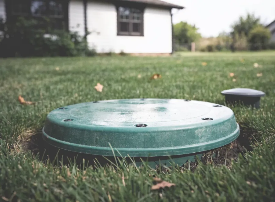 A green septic riser lid set flush in a mowed lawn at an Indiana home